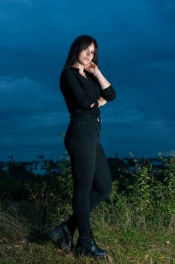 Güzel dikey portre. Şehvetli bir kadının görüntüsü, görkemli ve renkli, siyah elbiseli, şehrin arka planında poz veren.