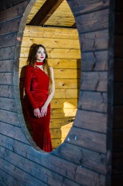 Güzel dikey portre. Şehvetli bir kadının görüntüsü, yüksek ve renkli, kırmızı elbiseli, ahşap bir odada poz veriyor..