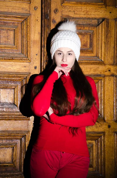 美丽的垂直肖像 穿着红色毛衣和裤子的女孩靠近木门 — 图库照片
