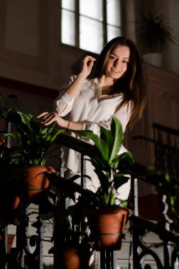 Ön planda saksıları olan, beyaz elbiseli bir kızın dikey portresi..