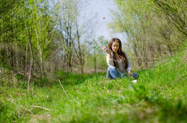 Ormanda çimlerin üzerinde oturan bir kızın yatay portresi..