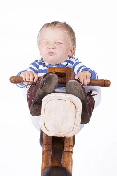 Boy grimacing on wooden motorbike — Stock Photo, Image