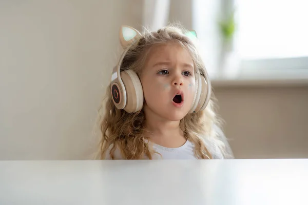 Cute little girl listens to music in childrens headphones at home — Stock Photo, Image