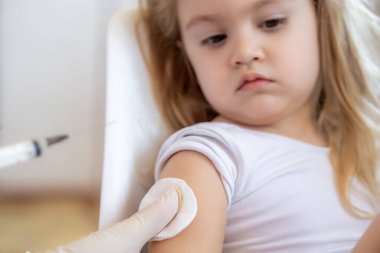 Çocuk bağışıklığı kavramı. Küçük sevimli sarışın kız oyuncak tutuyor ve grip aşısı oluyor şırınga iğnesinden korkmuyor. Doktor klinikte cesur çocuğa Covid-19 aşısı enjekte ediyor.