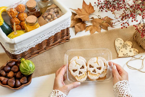 Female hands packing Halloween presents. Some spice, chestnuts, scull biscuits, panelles de piones in craft gift box. Healthy zero waste life style. Ethical shopping ideas, eco friendly and diy concept.