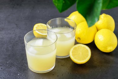 Gri arka planda bir bardak limon suyu ve taze olgun limonlar. Sağlıklı meyve yeme konsepti.