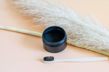 Tarafsız bej arka planda organik kömür ve bambu diş fırçası, otlar ve doğal dekoratif elementler olarak kamış bambu içeren bir kutu. Diş beyazlatma, refah kavramları.
