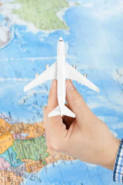 Studio shot of toy plane in hand with world map on background - travelling concept — Stock Photo, Image