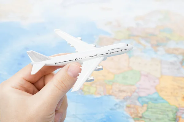 Studio shot of toy plane in hand with world map on background - focus on the plane — Stock Photo, Image