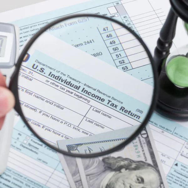 Close up studio shot of USA 1040 Tax Form with magnifying glass and hourglass — Stock Photo, Image