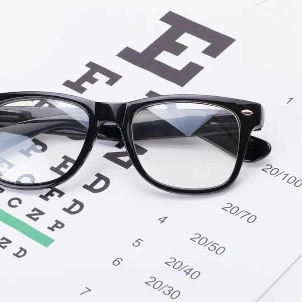 Chiuda sul colpo di studio di una tabella di prova di vista e occhiali sopra esso — Foto Stock