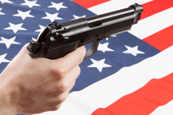 Gun in hand with ruffled national flag on background - United States — Stok Foto