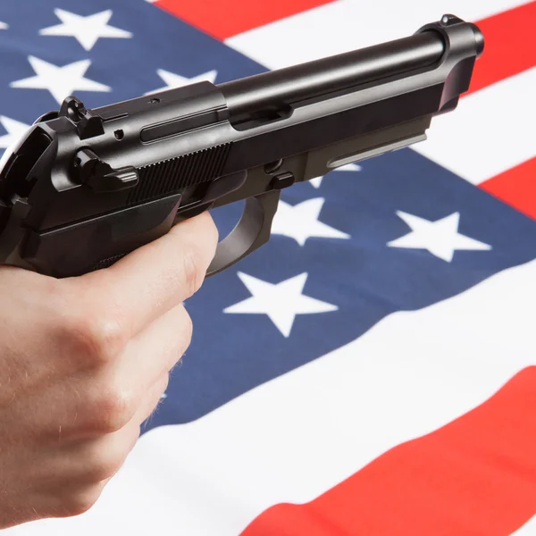 Închideți o fotografie de studio a unei arme în mână cu steagul național pe fundal - Statele Unite ale Americii — Fotografie, imagine de stoc