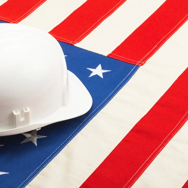 Close up studio shot of a white color construction helmet laying over US flag — Fotografia de Stock