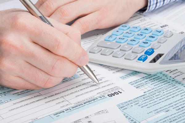 Un hombre llenando los E.e.u.u. impuesto 1040 forman con dólares y calculadora aseado —  Fotos de Stock