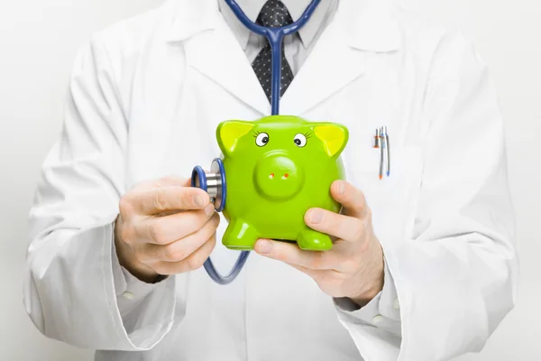 Doctor holding stethoscope and piggybank in hand — Stock Photo, Image