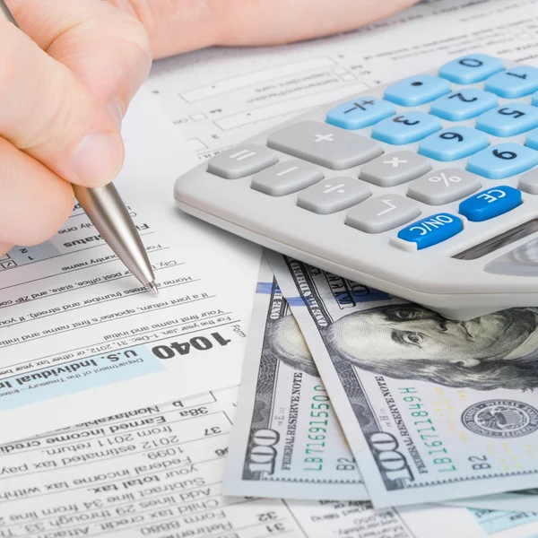 Hombre llenando 1040 nos impuestos con calculadora y dinero sobre la mesa - relación 1 a 1 —  Fotos de Stock