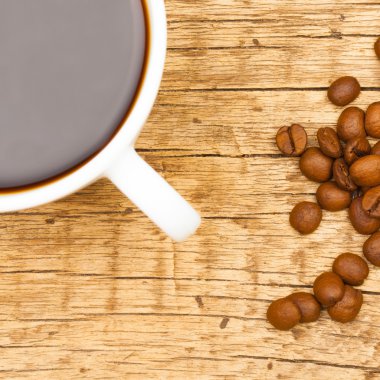 Close up of neat coffee cup with roasted coffee beans on wooden table - view from top clipart