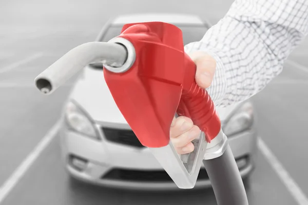 Red color fuel pump gun in hand with car on background — Stock Photo, Image