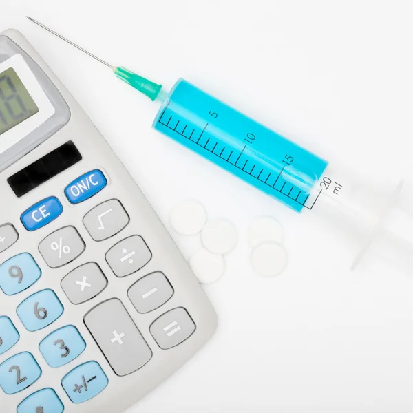 Calculator and a syringe with blue liquid inside - studio shot — Stock Photo, Image