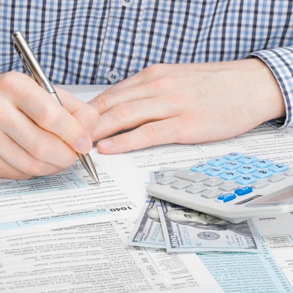 Мужчина, заполняющий 1040 нас налоговая форма с калькулятором и 100 долларов рядом с ним — стоковое фото