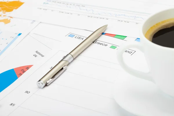 Кавова чашка і ручка над фінансовими картами — стокове фото