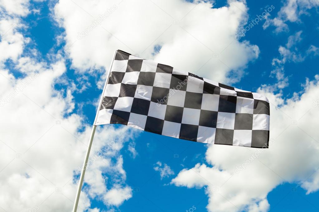 Checkered flag waving in the wind with clouds on background - outdoors shoot