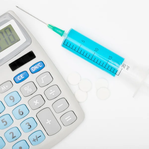 Calculator and a syringe with blue liquid inside — Stock Photo, Image