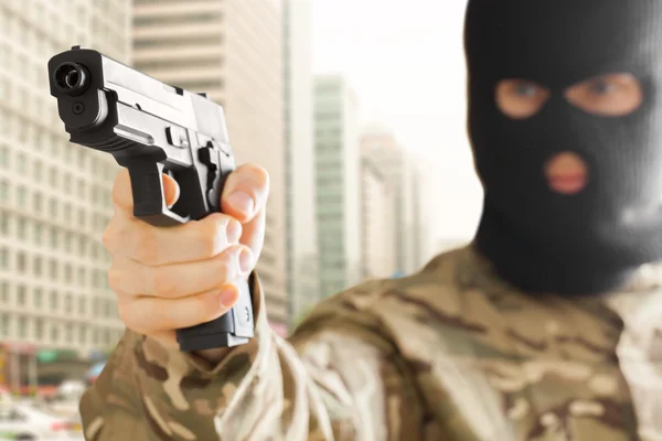 背景の都市が付いている銃を保持している黒い仮面の男 — ストック写真
