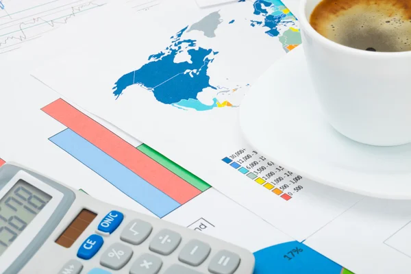 Coffee cup and calculator over world map and financial graphs — Stock Photo, Image