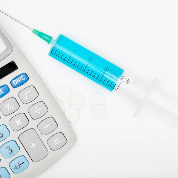 Calculator and a syringe with blue liquid inside - studio shot — Stock Photo, Image