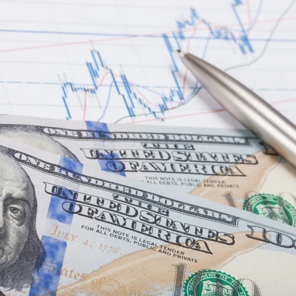 Графік фондового ринку з ручкою і банкнотою в сто доларів крупним планом — стокове фото