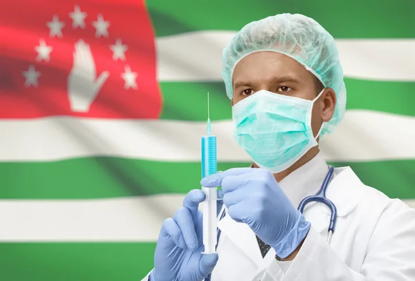 Doktor s injekční stříkačkou v ruce a vlajku na pozadí řady - Abcházie — Stock fotografie