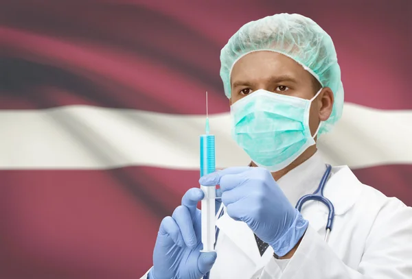 Doktor s injekční stříkačkou v ruce a vlajku na pozadí řady - Lotyšsko — Stock fotografie