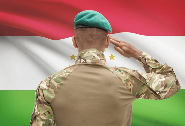 Dark-skinned soldier with flag on background - Tajikistan — Stock Photo, Image