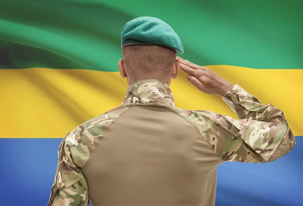 Dark-skinned soldier with flag on background - Gabon — Stock Photo, Image