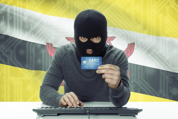 Dunkelhäutige Hacker mit Flagge auf Hintergrund hält Kreditkarte - Brunei — Stockfoto