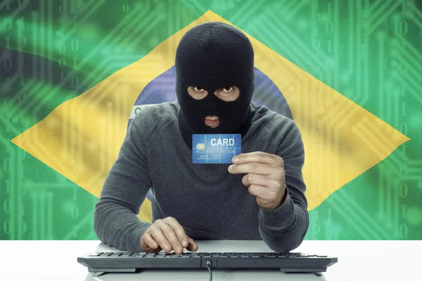 Dark-skinned hacker with flag on background holding credit card - Brazil — 图库照片