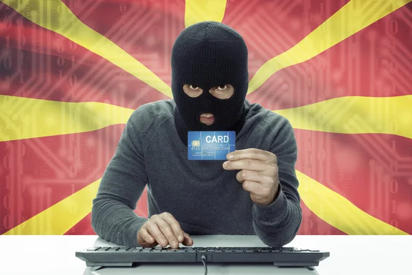 Dark-skinned hacker with flag on background holding credit card - Macedonia — стокове фото