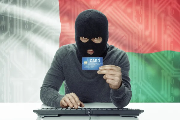 Dark-skinned hacker with flag on background holding credit card - Madagascar — Stock Photo, Image
