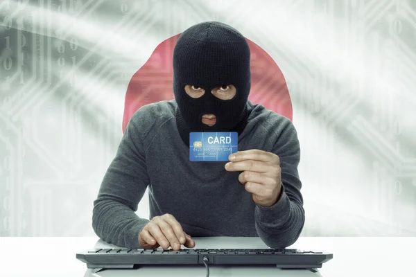 Dark-skinned hacker with flag on background holding credit card - Japan — стокове фото