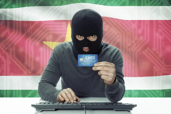 Dark-skinned hacker with flag on background holding credit card - Suriname — Stock Photo, Image