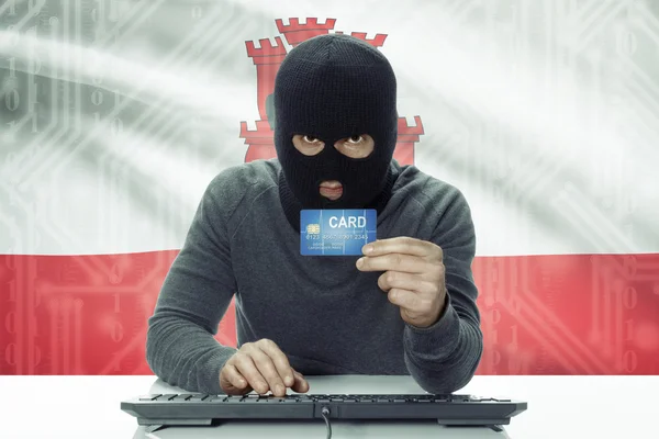 Dark-skinned hacker with flag on background holding credit card - Gibraltar — ストック写真
