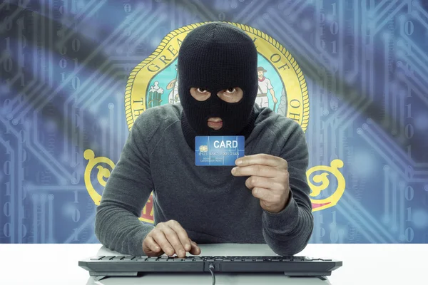 Dark-skinned hacker with USA states flag on background holding credit card - Idaho — стокове фото