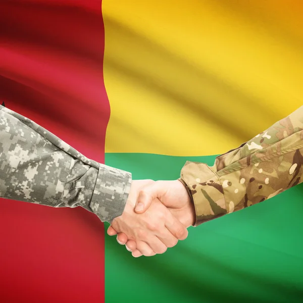 Men in uniform shaking hands with flag on background - Guinea-Bi — Stock Photo, Image