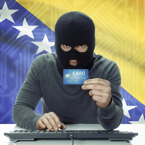 Dark-skinned hacker with flag on background holding credit card in hand - Bosnia and Herzegovina — 图库照片