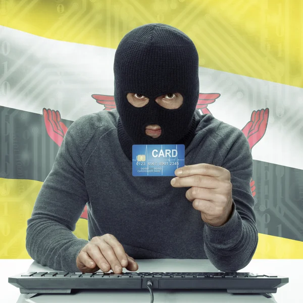 Dark-skinned hacker with flag on background holding credit card in hand - Brunei — Foto Stock