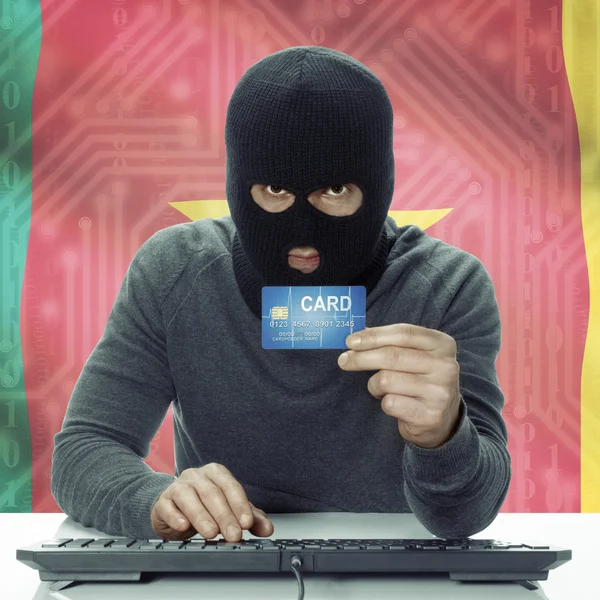 Dark-skinned hacker with flag on background holding credit card in hand - Cameroon — Stock fotografie