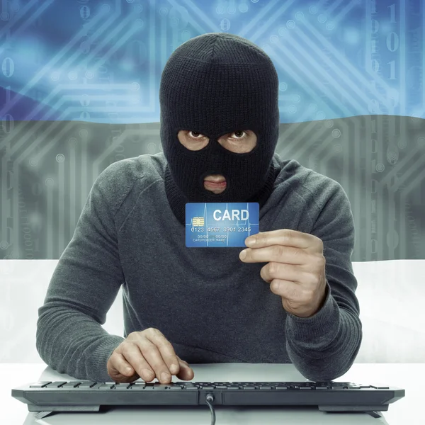 Dark-skinned hacker with flag on background holding credit card in hand - Estonia — Stock Photo, Image