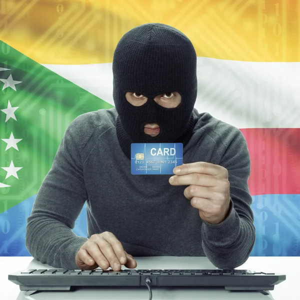 Dunkelhäutige Hacker mit Flagge auf Hintergrund mit Kreditkarte in der Hand - Komoren — Stockfoto